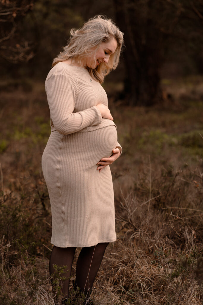 Een zwangere vrouw kijkt liefdevol naar haar buik tijdens een zwangerschapsshoot in de omgeving van apeldoorn