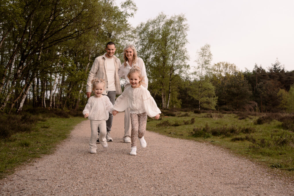 vader en moeder lopen hand in hand terwijl de twee dochters voor hen uit rennen.