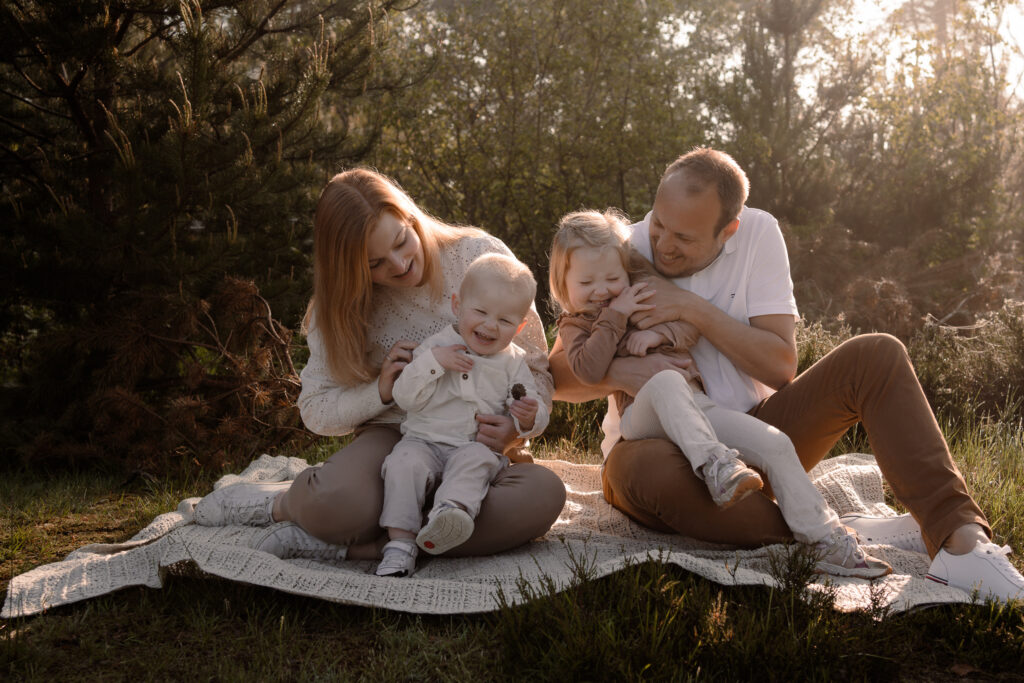 gezin zit op de grond en kietelen de kinderen terwijl de zon van achteren schijnt tijdens een gezinsshoot in de lente