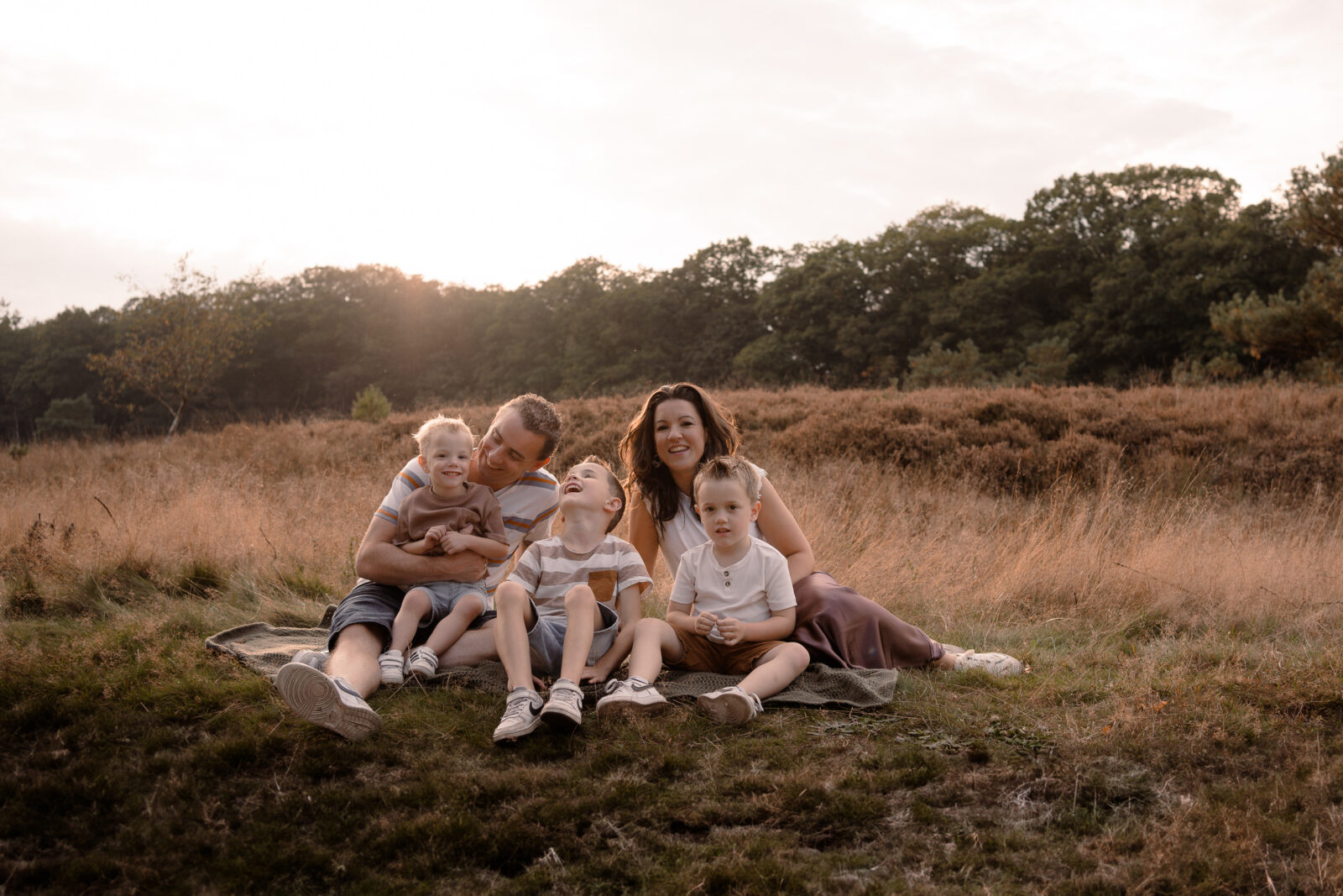 Een gezin zit op een kleedje en heeft plezier met elkaar tijdens een gezinsshoot in Apeldoorn met zonsondergang