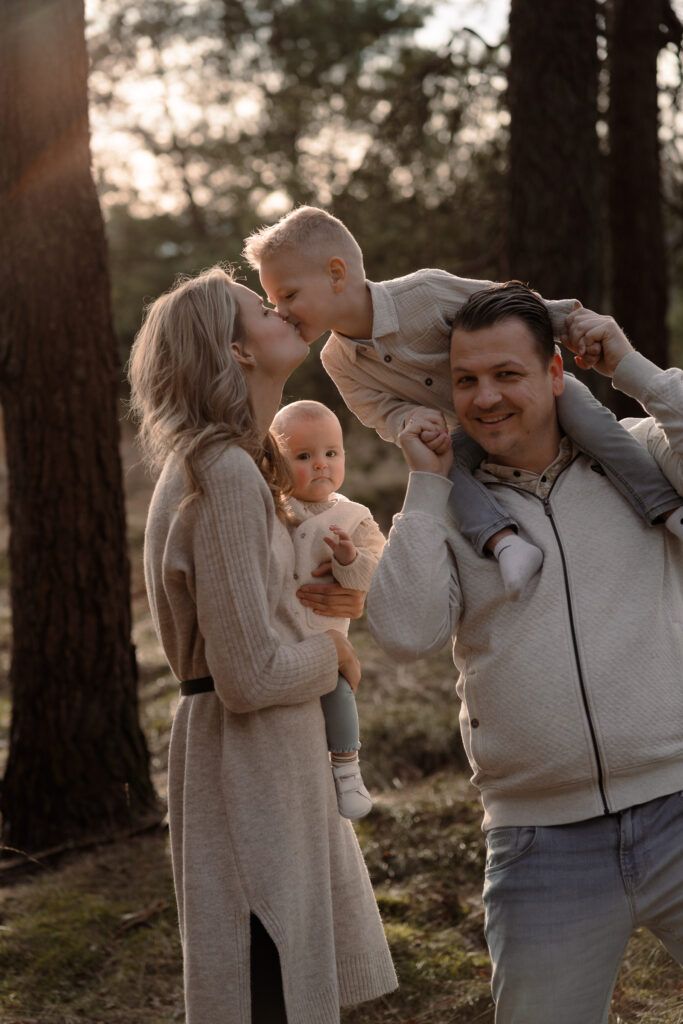 Zoon geeft moeder een kus tijdens een gezinsshoot met zonsondergang in de natuur