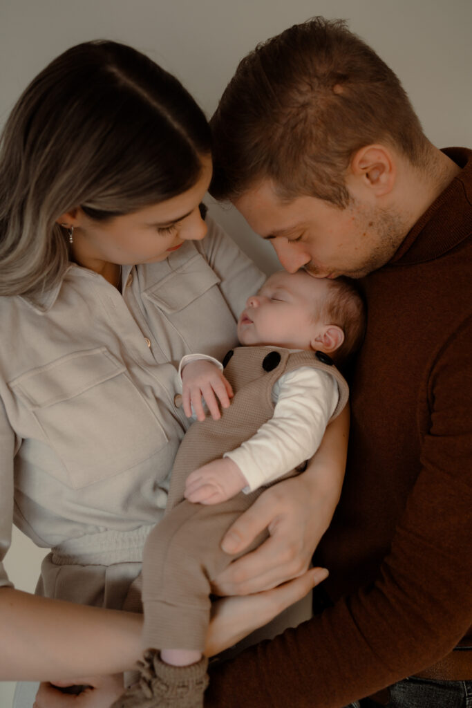 moeder draagt baby terwijl vader de baby een kus op zijn hoofdje geeft