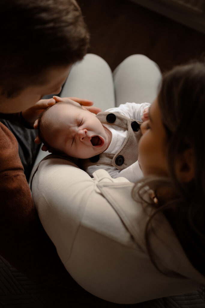 Een baby die uitgebreid gaapt terwijl hij tussen papa en mama ligt tijdens een newbornshoot