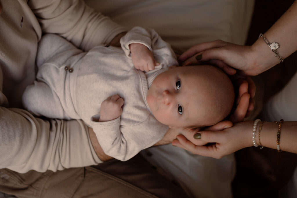 Baby liggen op papa's armen en mama's handen tijdens een newbornshoot thuis