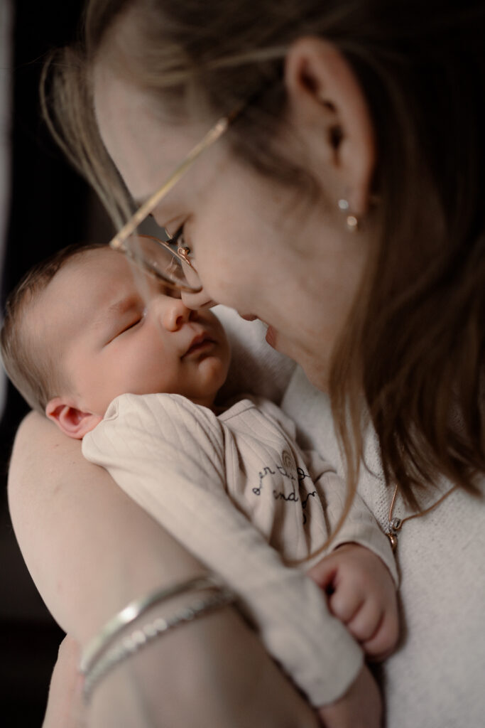 Moeder neust met haar kleine baby tijdens een newbornshoot thuis