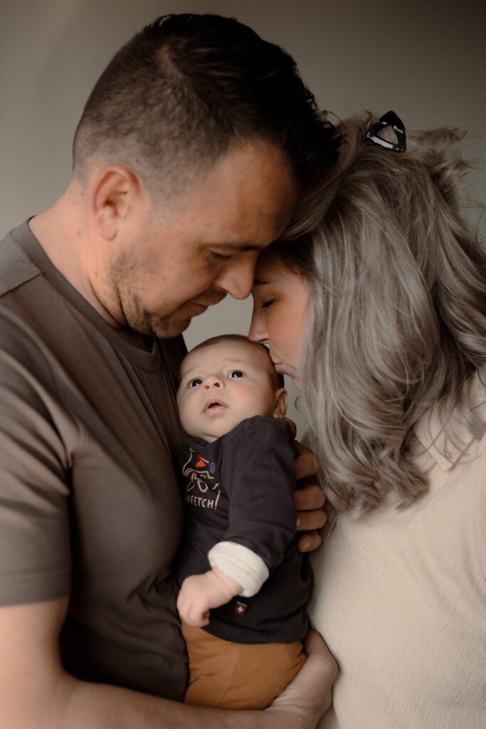 Baby tussen papa en mama terwijl mama een kus geeft tijdens een newbornshoot aan huis