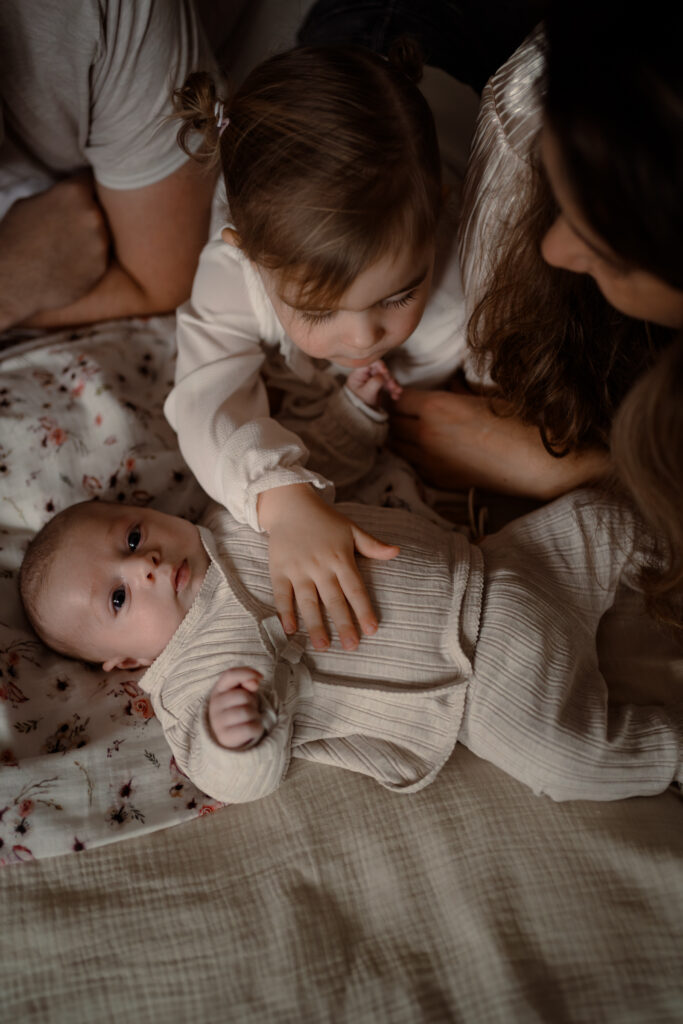 Grote zus aait babyzusje over haar buikje met een newbornshoot