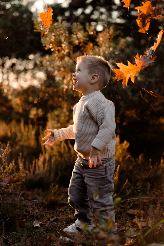 Een jongen speelt met de bladeren tijdens een gezinsshoot in herfst.