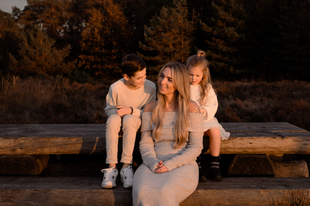 moeder met zoon en dochter zitten in de laatste zonnestralen van de ondergaande zon tijdens een gezinsshoot in de herfst 