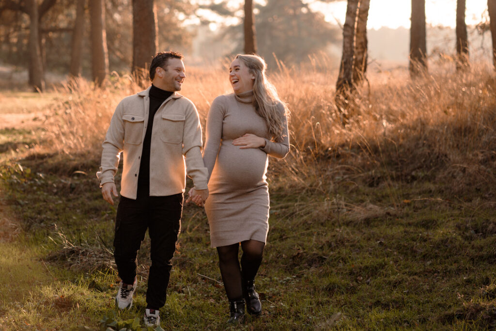 Zwangerschapsfoto van een vrouw en haar man die samen lachend wandelen in het bos op de Veluwe gefotografeerd door Joenne Bokhorst Fotografie