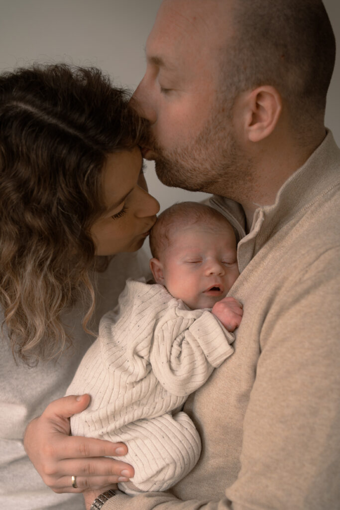 Moeder geeft pasgeboren zoontje een kus en vader geeft moeder een kus tijdens een newbornshoot Apeldoorn