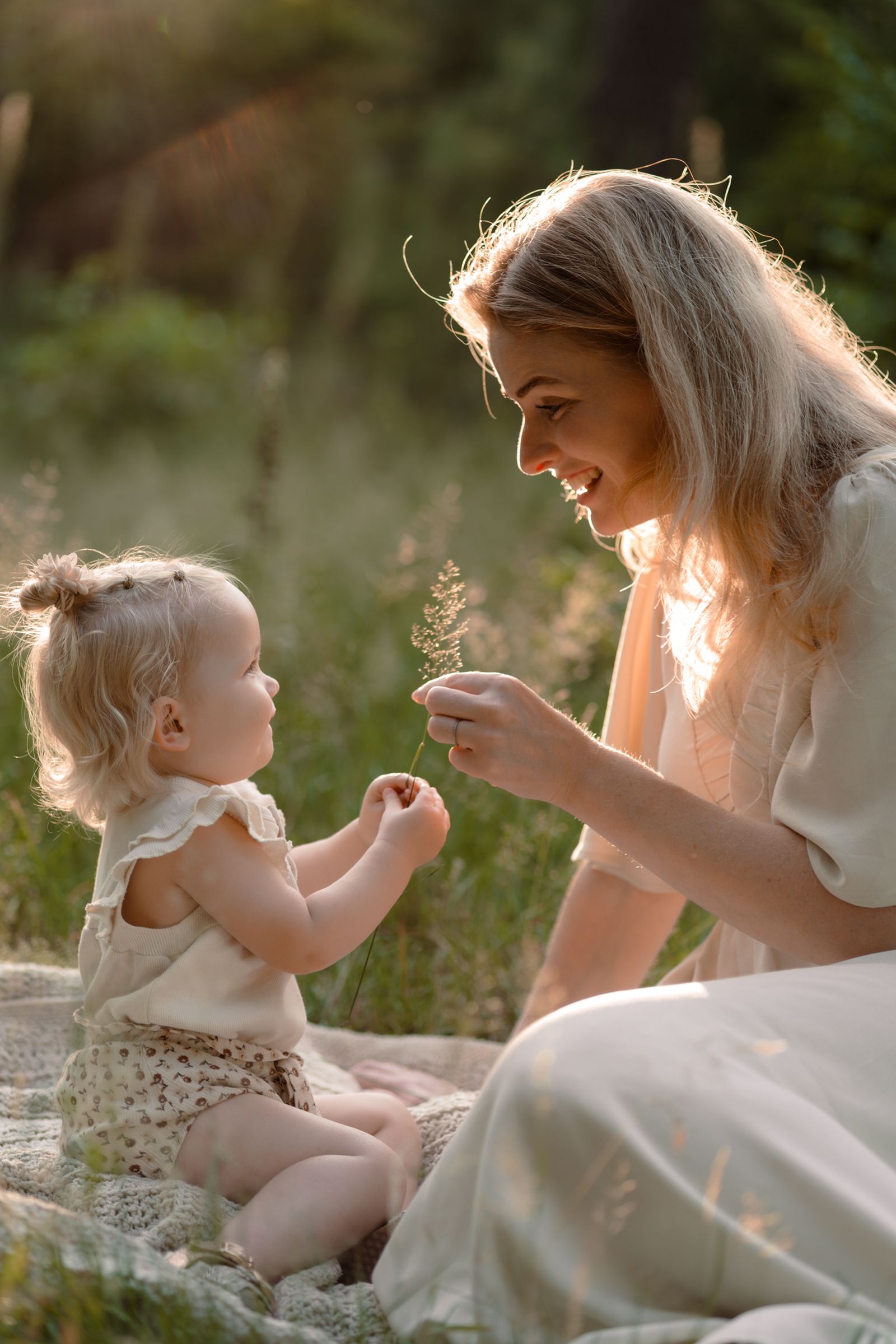 Moeder en dochtertje spelen met grassprietjes tijdens een gezinsshoot door Joenne Bokhorst Fotografie
