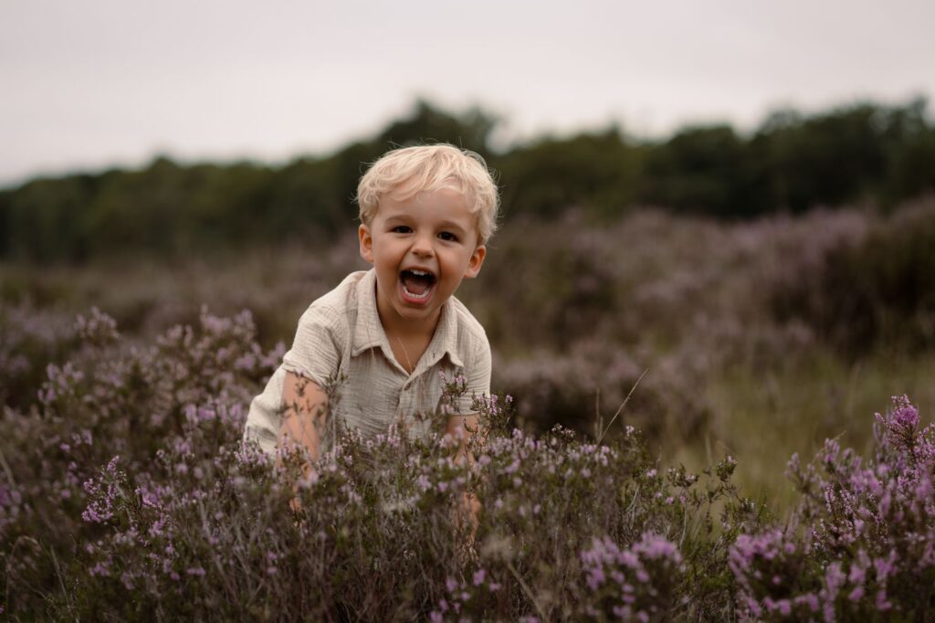 Jongetje die uit de bloeiende heide springt tijdens een fotoshoot door Joenne Bokhorst Fotografie