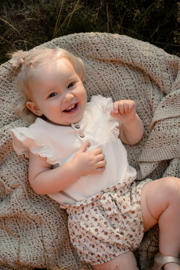 Lachende peuter liggend op een gebreid kleed buiten, kinderfotoshoot door Joenne Bokhorst fotografie
