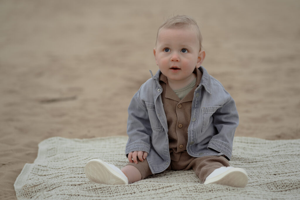 Baby zittend op een gebreid kleed op het zand tijdens een gezinsfotoshoot op het Kootwijkerzand gemaakt door fotograaf in Apeldoorn Joenne Bokhorst Fotografie