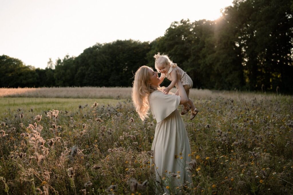 Moeder tilt lachende dochter op in een bloemenveld tijdens het gouden uur, gezinsfotoshoot door Joenne Bokhorst fotografie