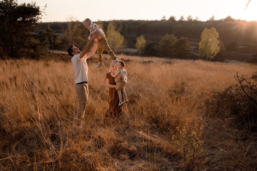 Hele gezin op de veluwe waarbij papa zoon in de lucht gooit.