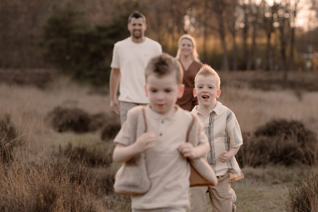 Kinderen rennen voor ouders uit over de heide tijdens een gezinsshoot met zonsondergang