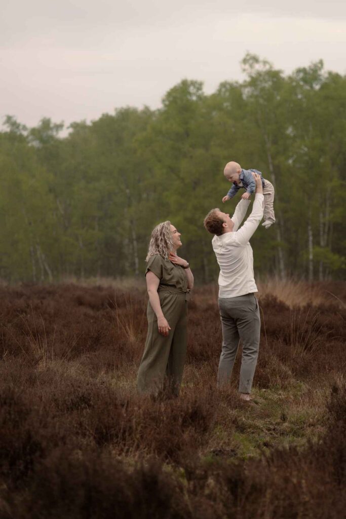 Gezin met baby op de heide tijdens gezinsshoot, mama in groene jurk en papa in crème sweater