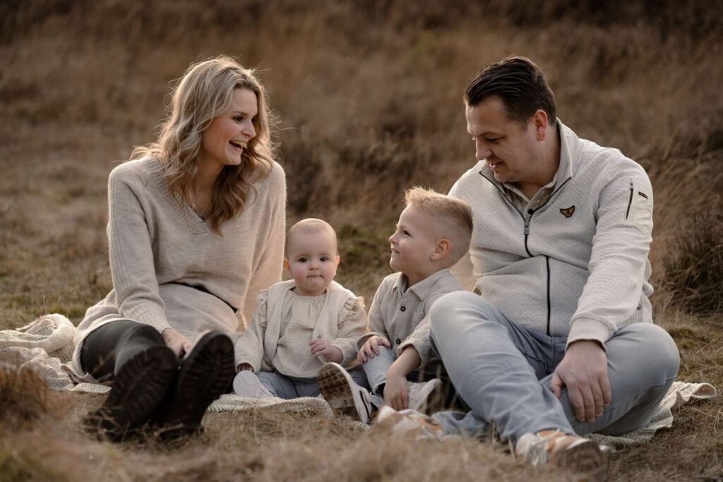 Gezin van vier zittend op een deken in het veld tijdens gezinsshoot, allemaal in neutrale beige en crème tinten